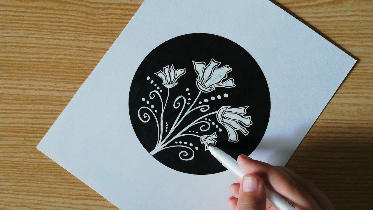 Motif floral blanc dessiné au feutre dans un cercle noir sur papier blanc